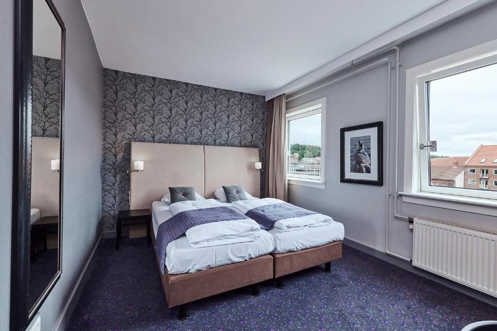 A twin-bed hotel room with a tall padded headboard and a window onto neighbouring roofs.