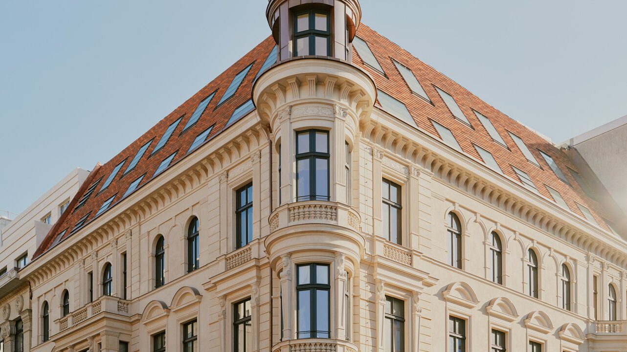 A cream stone corner building with a turret and a tiled roof on a city street.