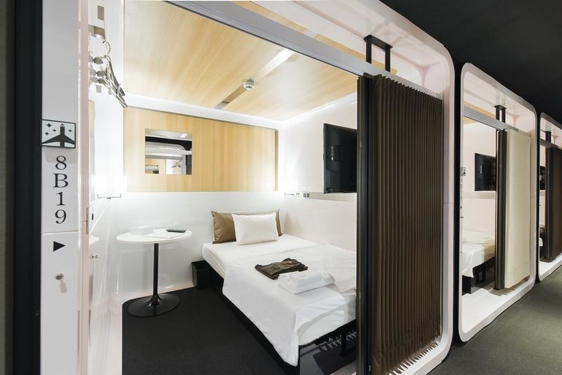 An open sleeping cabin in a row, with a bed, a small table and a screen at the entrance.
