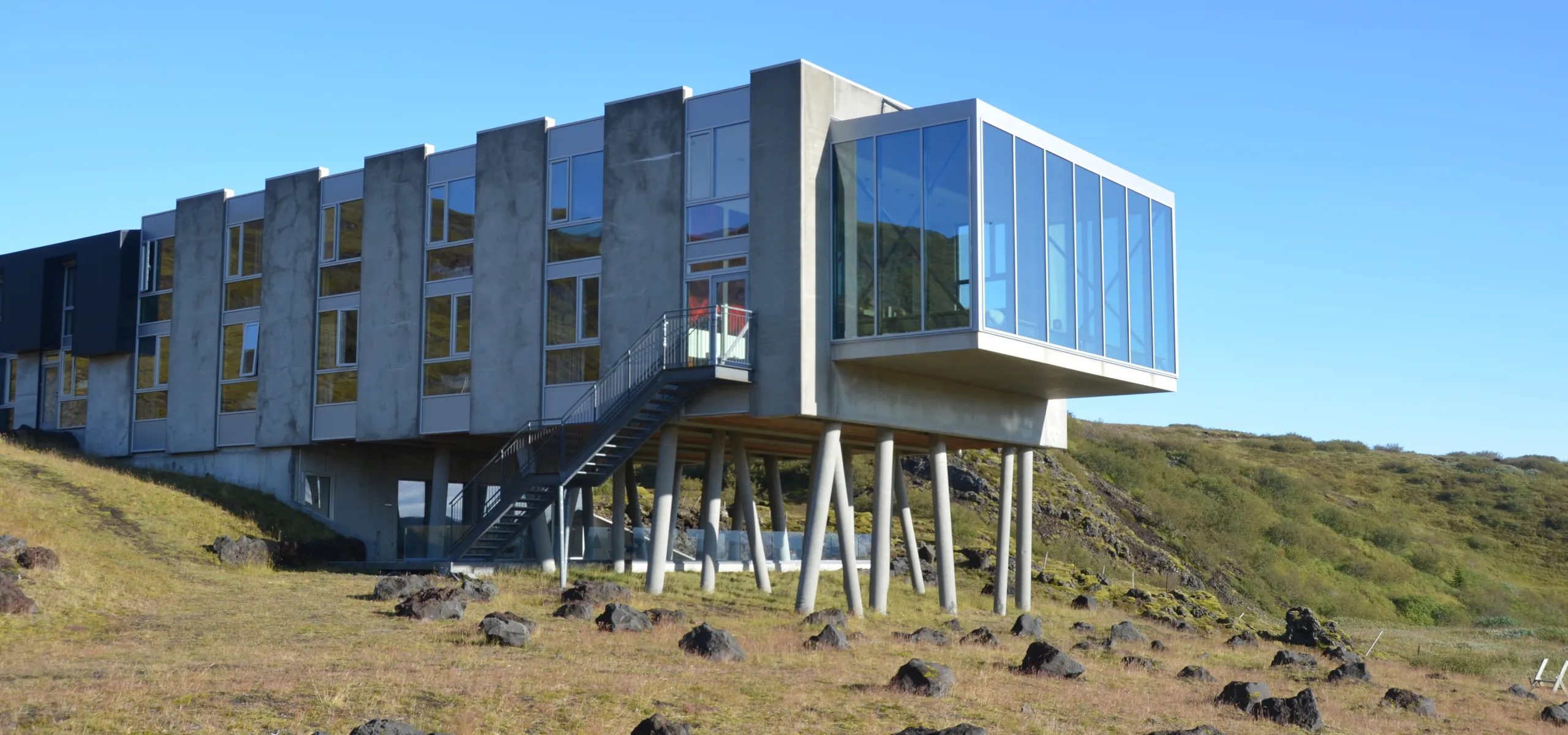 A long concrete hotel wing raised on angled supports above a rocky lava slope.