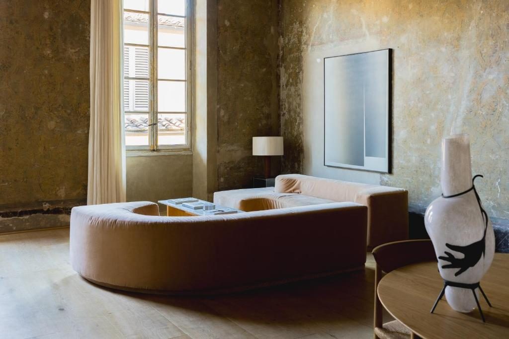 A high room with plastered walls, a curved sofa and a tall window.