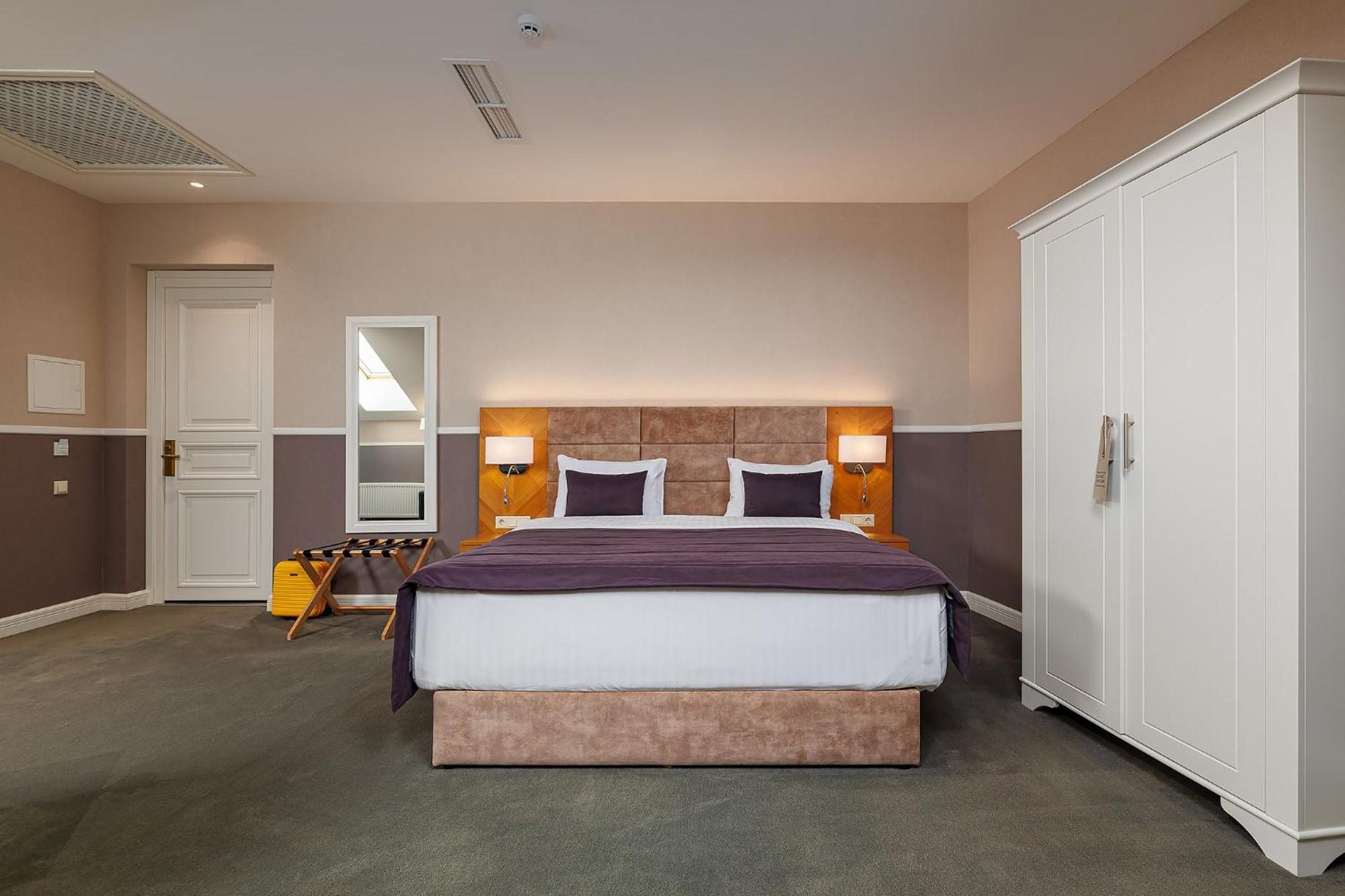 A plainly finished hotel bedroom with a padded headboard, a white wardrobe and a suitcase on a rack.