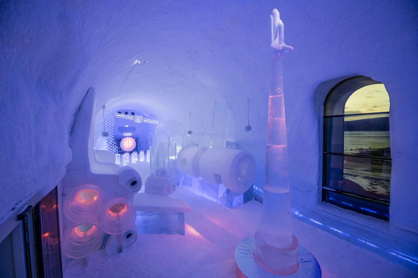 A vaulted room carved from snow and ice, lit in blue, with ice sculptures along the walls.