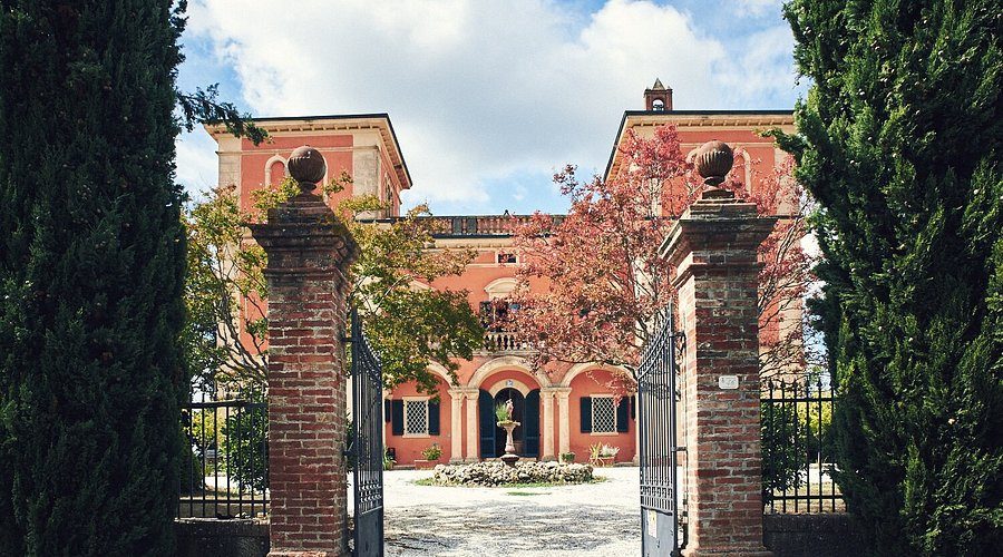 A terracotta villa with twin towers seen through an open brick gateway.