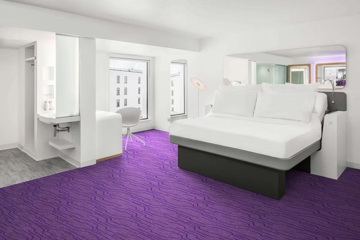 A compact white cabin with a fitted bed, a desk at the window and a purple floor.